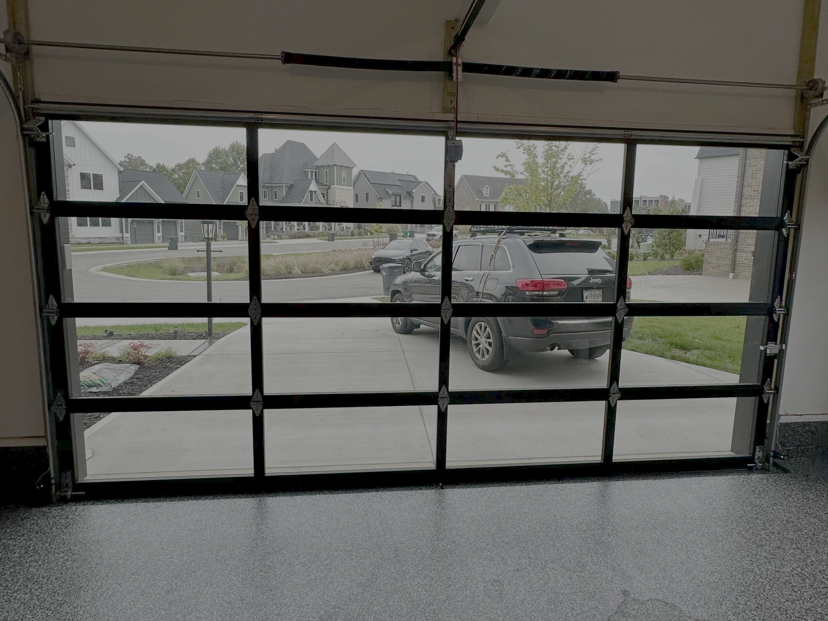 View from inside a garage with clear glass doors, showing the outside.